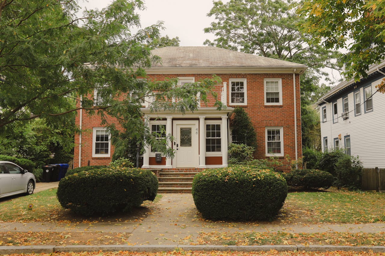 who-we-are Charming red brick house with a well-maintained front garden and greenery.
