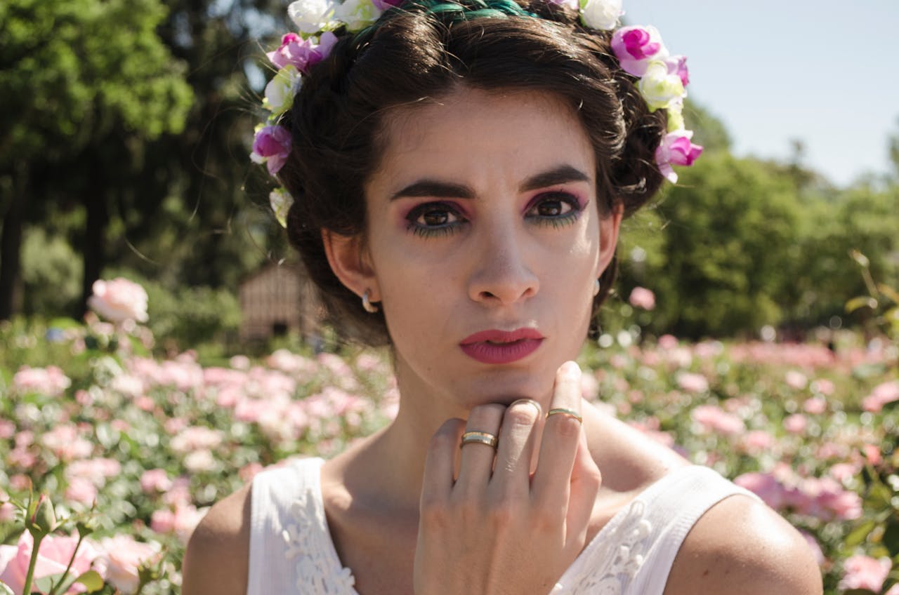 contact-img Portrait of a young woman with a flower crown surrounded by blooming flowers in a park setting.